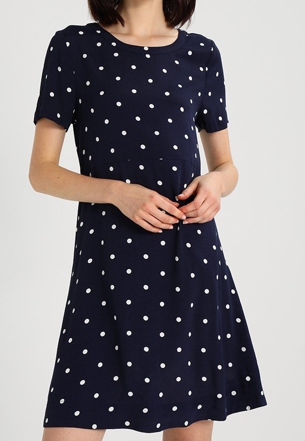 Námořnické modré šaty s krátkým rukávem a bílými puntíky, s kulatým výstřihem a volně střiženou sukní, která se jemně rozšiřuje.
