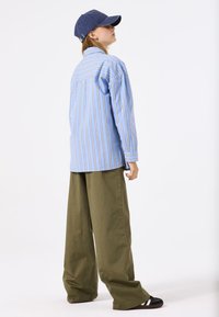 Blau-weiße gestreifte Langarmbluse mit lockerer Passform, kombiniert mit olivgrünen weiten Hosen und einer marineblauen Mütze.