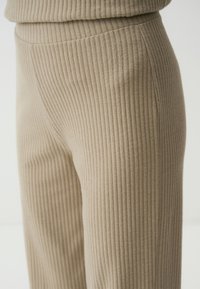Beige ribbed fabric trousers with a slight sheen, featuring a streamlined design and smooth texture, extending to a straight leg.