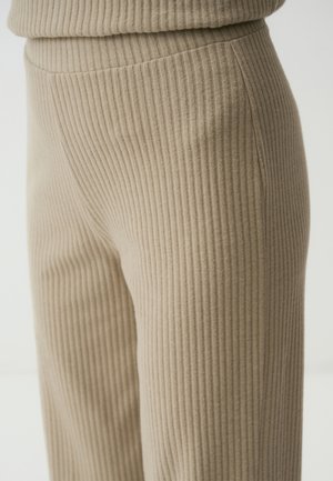 Pantaloni in tessuto a costine beige con una leggera lucentezza, caratterizzati da un design elegante e una texture liscia, che si estendono fino a una gamba dritta.