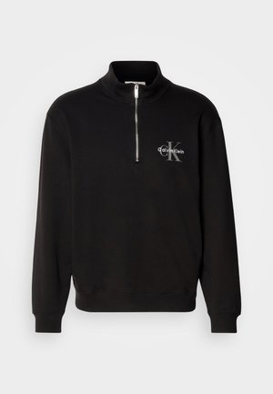Zwarte pullover met hoge kraag en kwart rits, met een grijze "Calvin Klein" logo en "K" embleem op de borst. Gemaakt van een katoenmix.