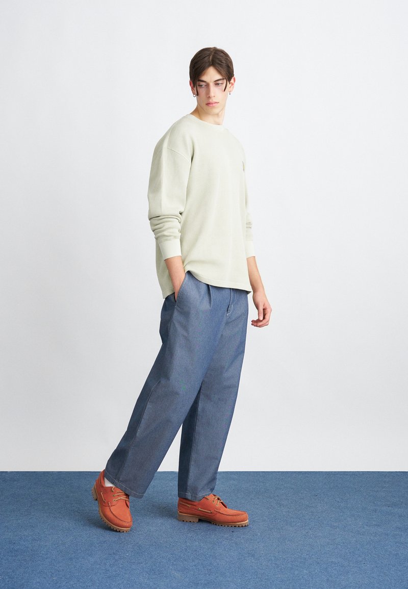 Lys grøn struktureret sweater, blå brede bukser og orange sko med snørebånd og gummisåler. Simpelt, afslappet fit design.