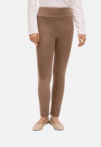 Leggings marrones con una textura suave y una cinturilla alta, con un ajuste ceñido y un diseño hasta el tobillo. Llevados con bailarinas beige.