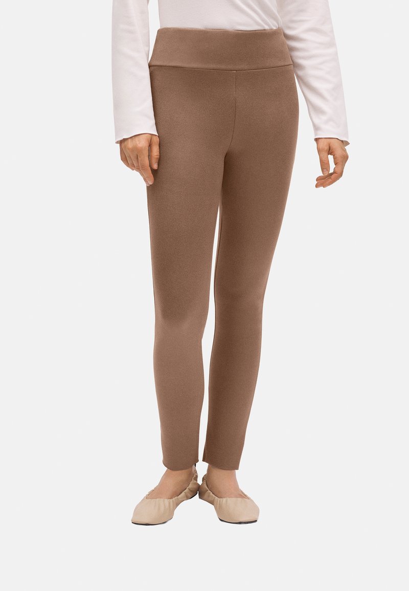 Leggings marrones con una textura suave y una cinturilla alta, con un ajuste ceñido y un diseño hasta el tobillo. Llevados con bailarinas beige.