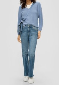 Lichtblauwe gebreide trui met v-hals, gecombineerd met een middelhoge was rechtgevallen jeans en witte platform sneakers. Schoudertas in bijpassend blauw.