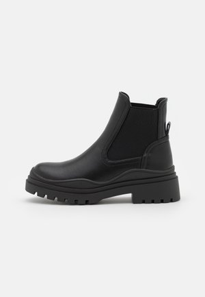 Bottine en cuir noir à cheville avec panneau latéral en élasthanne, tirant à l'arrière et semelle épaisse à crampons, présentée de l'extérieur sur fond blanc.