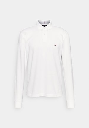 White long-sleeve polo shirt, cotton material, classic collar, two-button placket, small logo detail on the chest, ribbed cuffs.