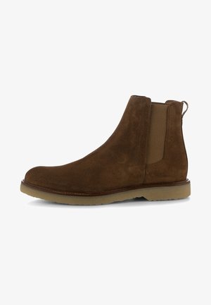 Bota Chelsea de ante marrón con panel lateral elástico y suela de goma beige, mostrada de perfil sobre un fondo blanco.