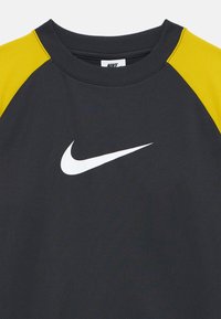 Sweatshirt Nike noir et jaune avec un col rond. Présente un logo swoosh blanc à l'avant, avec un design en color-block aux épaules.