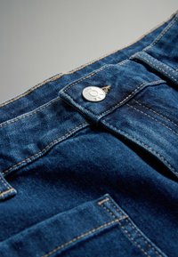 Dunkelblaue Denim-Jeans mit sichtbaren Nähten, einem Metallknopf mit der Aufschrift "THE SET" und einer Nahaufnahme des Taillenbunds und des Taschenbereichs.