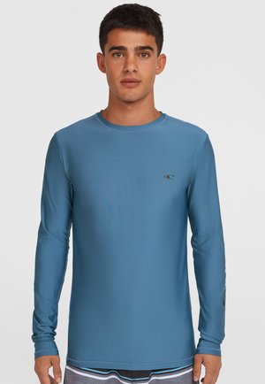 Chemise à manches longues de couleur bleue unie, avec un col rond et un accent de logo sur la poitrine. Fabriquée dans un tissu lisse et extensible.