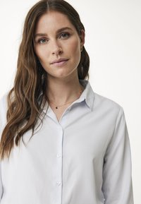 Ljusblå knapp-up-skjorta med mjuk textur, klassisk krage och långa ärmar, med transparenta knappar och en avslappnad passform.