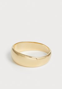 Bracciale in metallo dorato con un design liscio e arrotondato. Presenta una finitura lucida, una forma leggermente conica e un aspetto senza giunture.