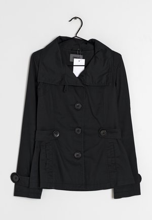 Black buttoned jacket with wide collar, belt-like details at waist and cuffs, hanging on a black hanger against a white background.