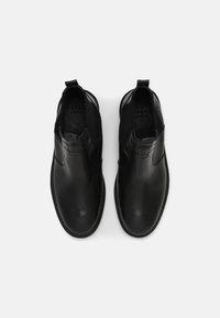 Pár černých kožených chelsea bot s kulatými špičkami a elastickými bočními panely, zobrazených shora na bílém pozadí.