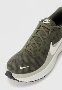 Baskets de course Nike en vert olive avec une tige en mesh texturé, des accents gris, un logo swoosh blanc et une semelle rembourrée. Semelle extérieure en caoutchouc noir.