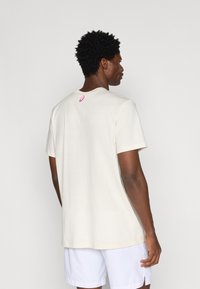 Κρέμα κοντομάνικη μπλούζα με στρογγυλή λαιμόκοψη, με μικρό ροζ λογότυπο στο πίσω μέρος, κατασκευασμένη από μαλακό, αναπνεύσιμο υλικό.