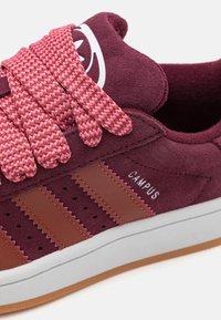 Burgundi bőr sneaker rózsaszín szőtt fűzőkkel, három barna bőr csíkkal és fehér logóval. Perforációkkal és gumi talppal rendelkezik.