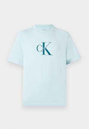 T-shirt de manga curta azul claro com grande logótipo "CK" em azul escuro e texto menor "Calvin Klein" centralizado na frente.
