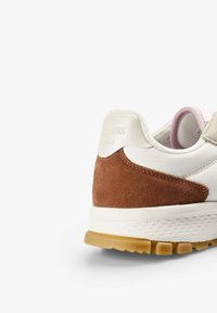 Sneaker featuring white leather upper, brown suede heel, and textured rubber sole. Notable soft pink accents on the inner lining.