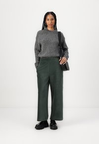 Maglione grigio chunky a collo alto, abbinato a pantaloni a gamba larga in suede verde scuro. Borsa a tracolla nera e scarpe nere chunky.