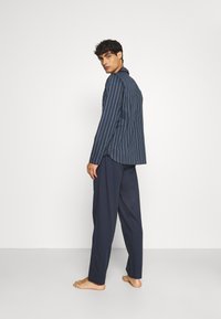 Camicia a maniche lunghe a righe blu navale abbinata a pantaloni rilassati blu scuro, con tessuti morbidi e design minimalista.