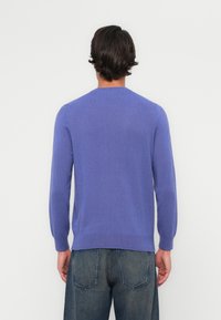 Lila Strickpullover mit langen Ärmeln und rundem Halsausschnitt. Weiche Textur mit glatter Oberfläche. Kombiniert mit dunklen Jeans.