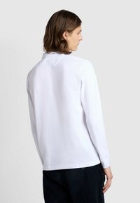 Camicia bianca a maniche lunghe con colletto classico, trama liscia e vestibilità sartoriale. Presenta un sottile dettaglio di cucitura nella parte posteriore.
