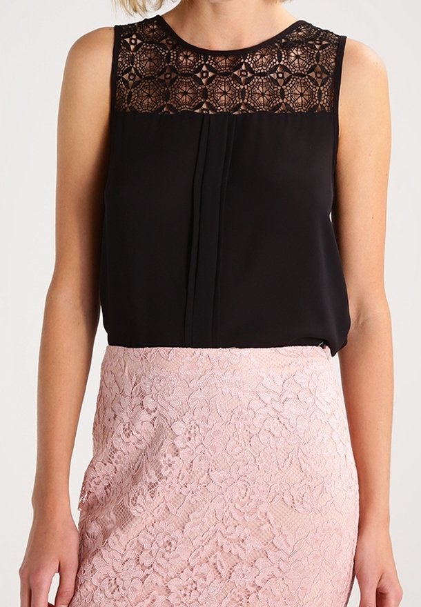 Blusa nera senza maniche con scollatura in pizzo, abbinata a una gonna aderente in pizzo rosa chiaro, che mette in risalto motivi e texture intricate.