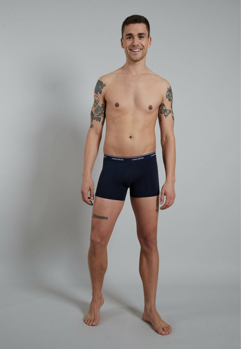 Navy blue boxer shorts made of smooth fabric, featuring a contrasting branded waistband, with a fitted design and soft texture.