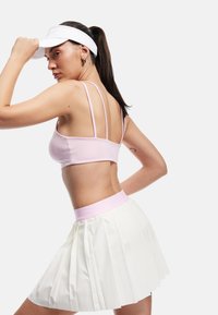 Sporty outfit med en lyserød, tætsiddende top med tynde stropper og en hvid, plisseret nederdel. En hvid skyggehue fuldender looket.