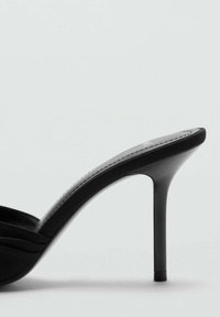 Mules negras de tacón alto con un diseño elegante, que presentan un empeine liso, una plantilla acolchada y una punta afilada, montadas sobre un fino tacón de aguja.