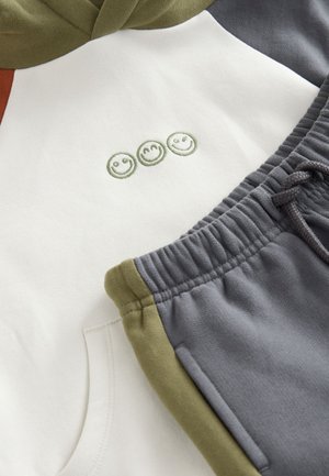 Bomuldshoodie med grønne og grå farveblokdesign, der har tre broderede smileyer; kombineret med grå fleece joggers med elastisk taljebånd.