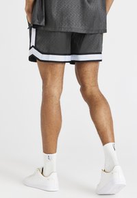 Shorts de sport noirs avec des bandes blanches sur les côtés, présentant un motif texturé. Portés avec des chaussures et des chaussettes blanches.