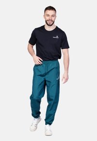 Pánsky outfit pozostávajúci z čierneho bavlneného trička a tyrkysových, ľahkých nohavíc s elastickým pásom a manžetami na členkoch, doplnený o biele tenisky.