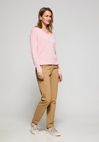 Ljusrosa kabelstickad tröja med V-hals, tillsammans med tanfärgade byxor och krämfärgade sneakers. Slät textur och avslappnad passform.