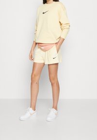 Nike sweatshirt i ljusgul med svart logotyp, matchat med gula shorts och en rosa midjeväska. Vita sneakers med rosa detaljer.
