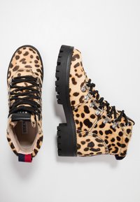 Bottines à imprimé léopard avec des lacets noirs, des œillets en aluminium et un matériau en fourrure texturé. Semelles en caoutchouc noir épaisses offrant durabilité.