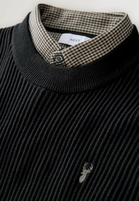 Maglione nero a coste con colletto a camicia a scacchi nero e beige. Presenta un piccolo design ricamato sul petto.