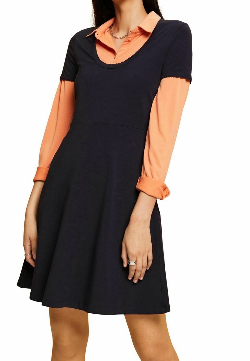 Granatowa sukienka z krótkimi rękawami na pomarańczowej bluzce, z okrąg�łym dekoltem i sylwetką w kształcie litery A. Gładki materiał i złożone mankiety.