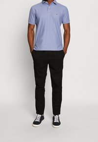 Ljusblå pikétröja i bomullsmix med klassisk krage, svarta avsmalnande byxor och marinblå sneakers med vita snören.