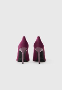 Vijolične visoke pete iz blaga z gladko teksturo, koničastim nosom in vitkim stiletto peto. Zadaj imajo čisto, minimalistično obliko.