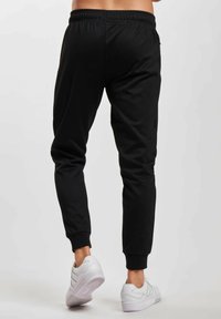 Pantalones de chándal negros con un corte ajustado y cinturilla elástica. Combinados con zapatillas deportivas blancas. Textura de tela suave, con un diseño minimalista.