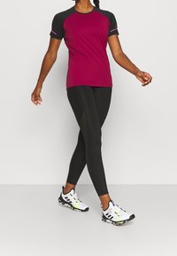 Bordowa koszulka z krótkim rękawem z czarnymi akcentami, zestawiona z czarnymi legginsami z panelami z siateczki. Białe i czarne buty sportowe z neonowymi akcentami.
