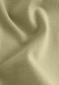 Bomullstyg i ljus olivgrön med en slät, elastisk textur och ett fint stickat mönster, som visar subtila veck och rynkor.