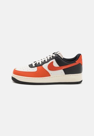 Low-top Nike sneaker med hvide, sorte og orange læderpaneler, hvide snørebånd og en orange Nike Swoosh på siden.