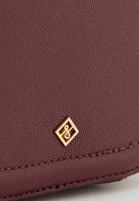 Bordo teksturirana kožna novčanica s malim zlatnim simbolom u obliku dijamanta, koja naglašava njezin elegantan dizajn i kvalitetu materijala.