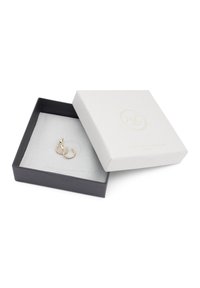 Goldfarbene Creolen mit klaren Verzierungen, präsentiert in einer schwarz-weißen Geschenkbox mit texturierter Oberfläche und bedrucktem Logo.