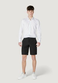 Camisa blanca de botones combinada con pantalones cortos negros y zapatillas blancas. El tejido parece suave y el diseño es simple y moderno.
