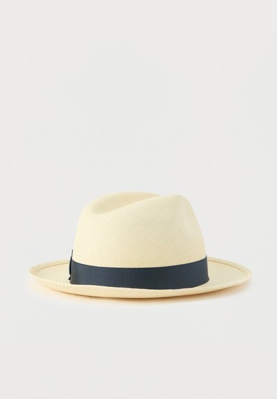Μπεζ ψάθινο καπέλο με φαρδύ γείσο και κορδέλα σε ναυτικό μπλε χρώμα. Η υφή είναι υφασμένη, με ομαλή, δομημένη σχεδίαση.